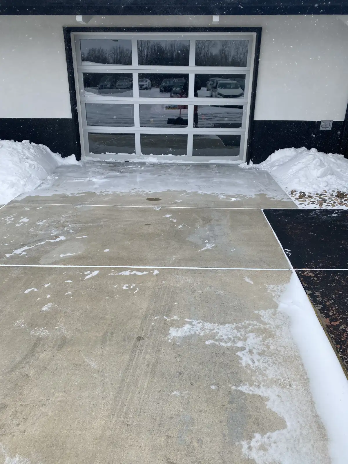 Concrete approach to a glass garage door with snow piled along both sides
